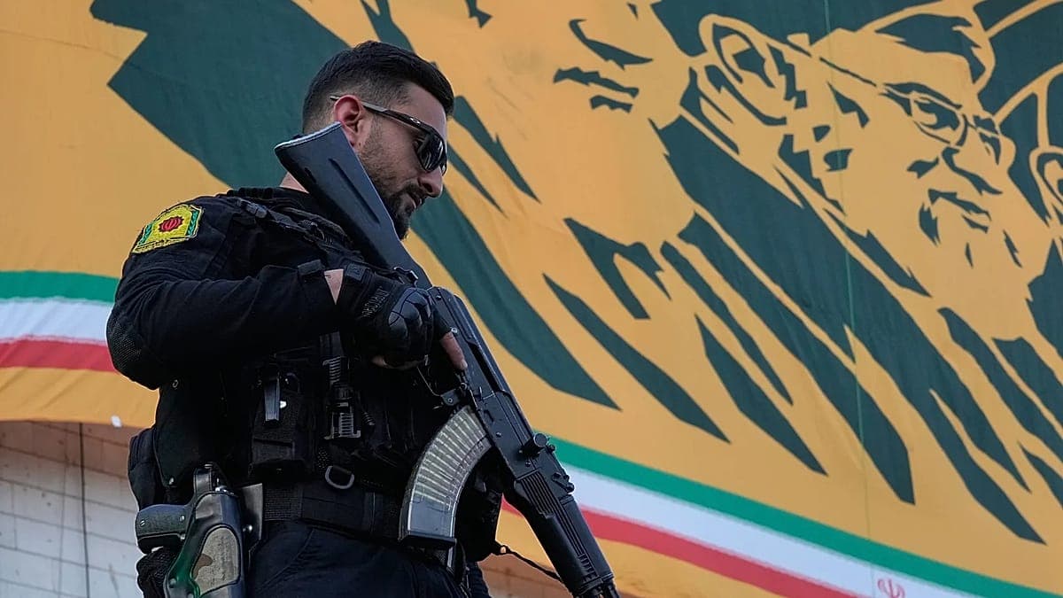 Seorang anggota pasukan keamanan berseragam hitam dengan insignia bahu berdiri di depan mural dinding berwarna kuning dan hijau dengan wajah terukir.