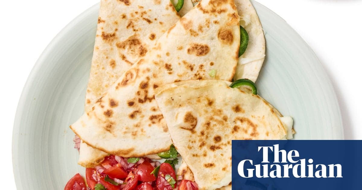 A white plate holds three quesadillas with golden-brown exterior char, filled with melted cheese, sliced green peppers, and topped with diced red tomatoes and fresh cilantro.