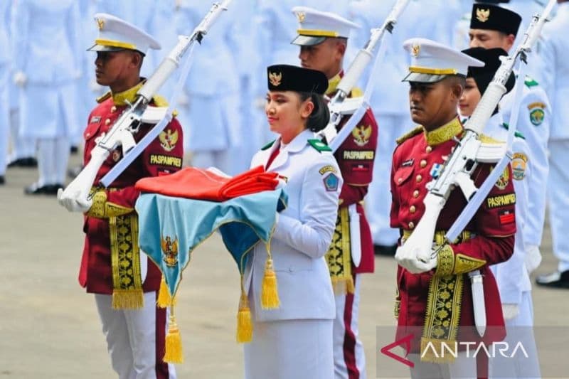Enam anggota Paskibraka dalam seragam formal merah dan putih membawa bendera merah putih Indonesia dengan postur tegak saat upacara.