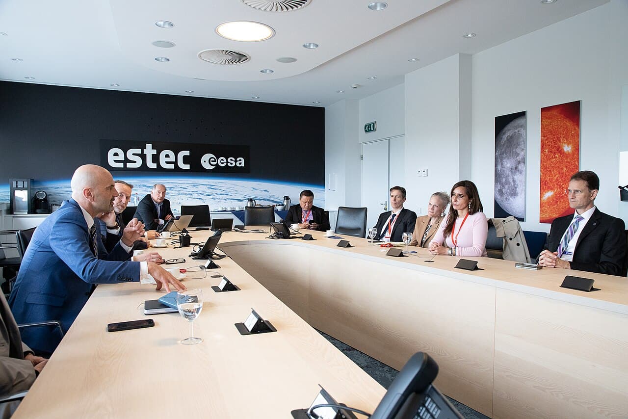 A group of professionals seated around a long conference table in a modern meeting room with the ESA and ESTEC logos displayed on the back wall.