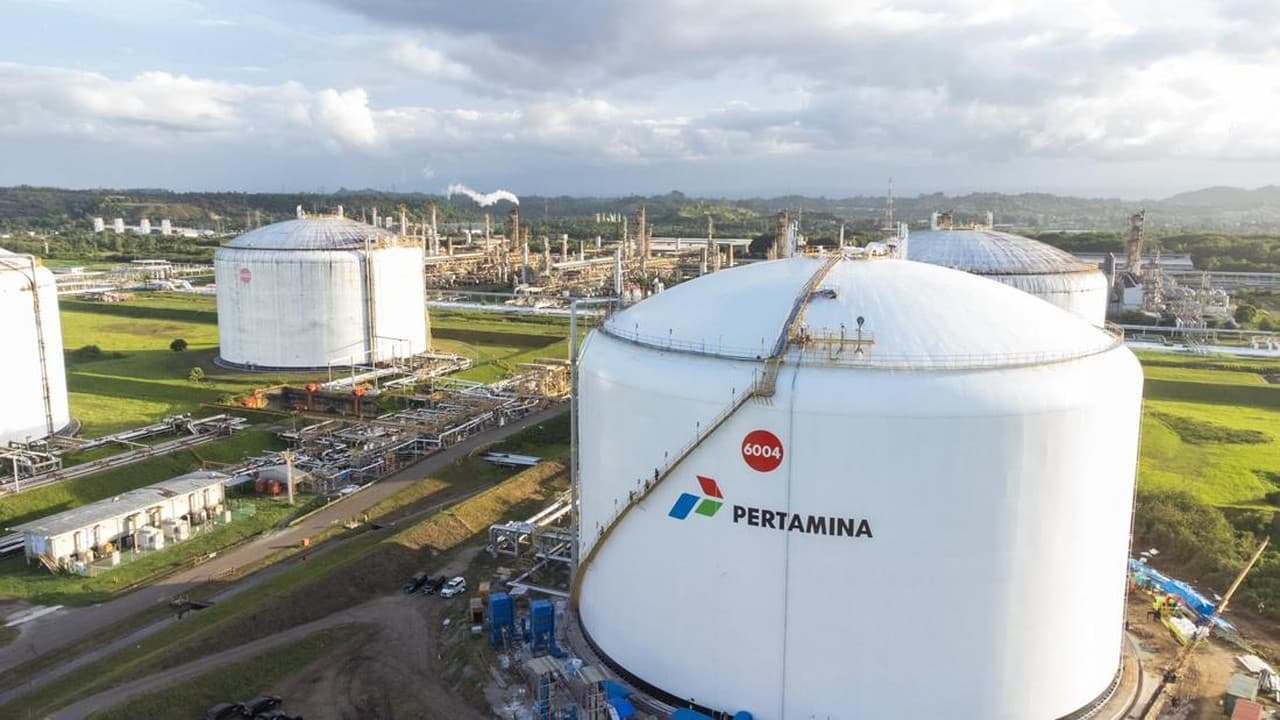 Fasilitas kilang minyak dan penyimpanan dengan tangki-tangki besar berwarna putih berlabel Pertamina yang tersebar di area industri yang luas dengan pemandangan pabrik di latar belakang.