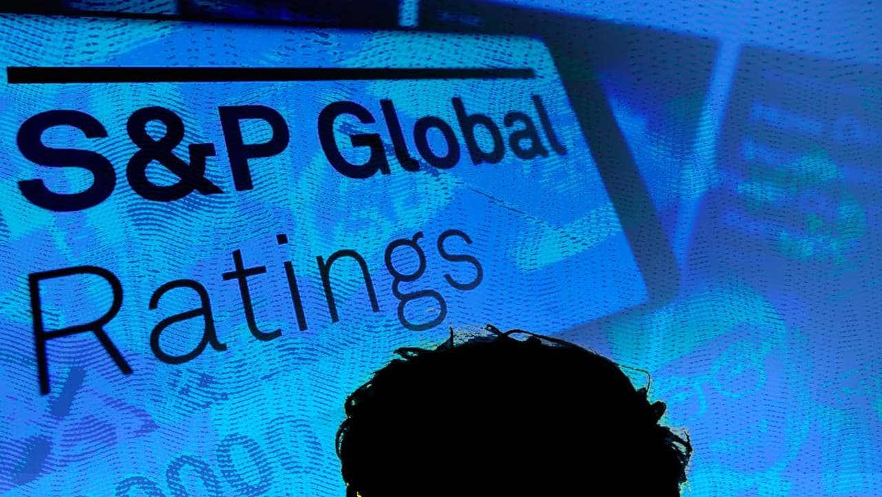 Layar komputer menampilkan logo dan teks "S&P Global Ratings" berwarna biru dengan bayangan kepala manusia di bagian bawah.
