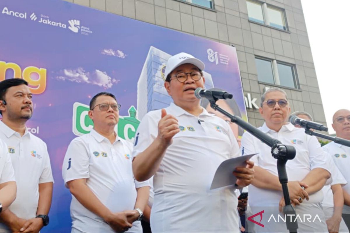 A government official speaking at a microphone with a purple banner backdrop reading "Ancol in Jakarta" at an official event in Jakarta.